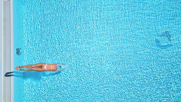 An aerial view of a swimming pool with clear blue water, a diving board, and a small boat. - Golfhotel Gutshof Penning (Rotthalmuenster)