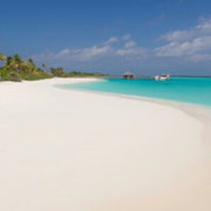 Ein Strand mit weißem Sand, klarem türkisblauem Wasser und einer kleinen Hütte in der Ferne.