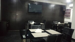 A conference room with a flat-screen TV mounted on the wall, several tables with chairs, and a dark-colored wall. - Maidaville Hotel and Suites (Lagos)