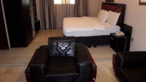 A hotel room with a large bed, a desk, a chair, and a wardrobe. - Maidaville Hotel and Suites (Lagos)