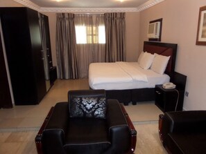 A hotel room with a large bed, a desk, a chair, and a wardrobe. - Maidaville Hotel and Suites (Lagos)