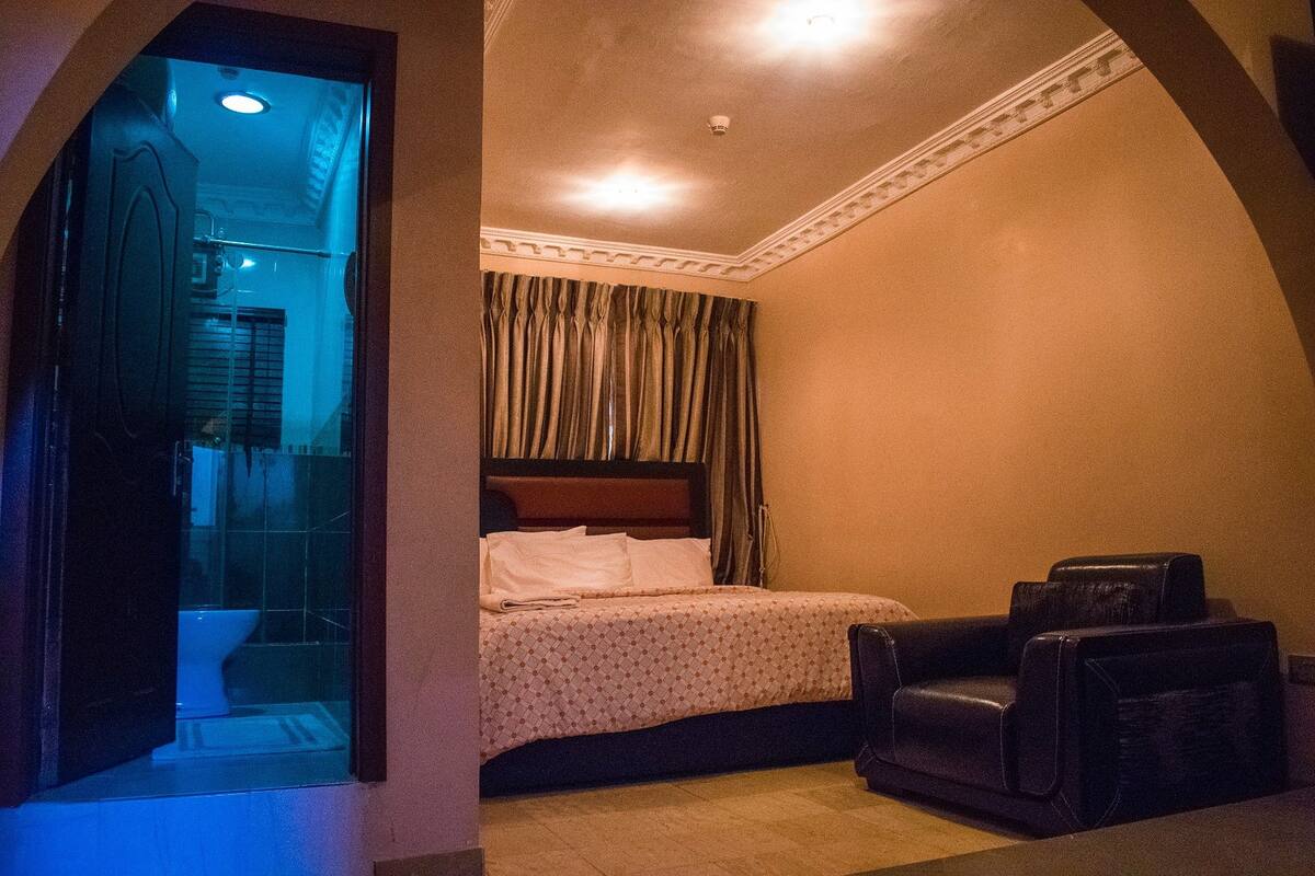 Quarto de hotel com cama, cadeira de massagem e banheiro visível por uma porta aberta.