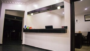 A reception area with a counter, a black chair, and a white wall with a framed picture. - Maidaville Hotel and Suites (Lagos)
