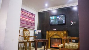 A room with a television mounted on the wall, a fireplace, and several wooden chairs. - Maidaville Hotel and Suites (Lagos)