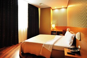 A hotel room with a bed, a nightstand with a lamp, a telephone, and a window with curtains. - Hotel Austria (Tirana)