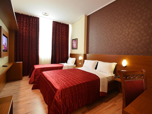A hotel room with two beds, a TV, a desk, and a wooden headboard. - Hotel Austria (Tirana)