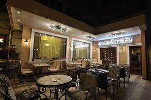 An outdoor seating area with tables and chairs, a large window with curtains, and a sign for 'HOTEL Austria'. - Hotel Austria (Tirana)