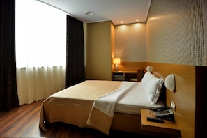 A hotel room with a bed, bedside table, lamp, and a view of the outdoors. - Hotel Austria (Tirana)