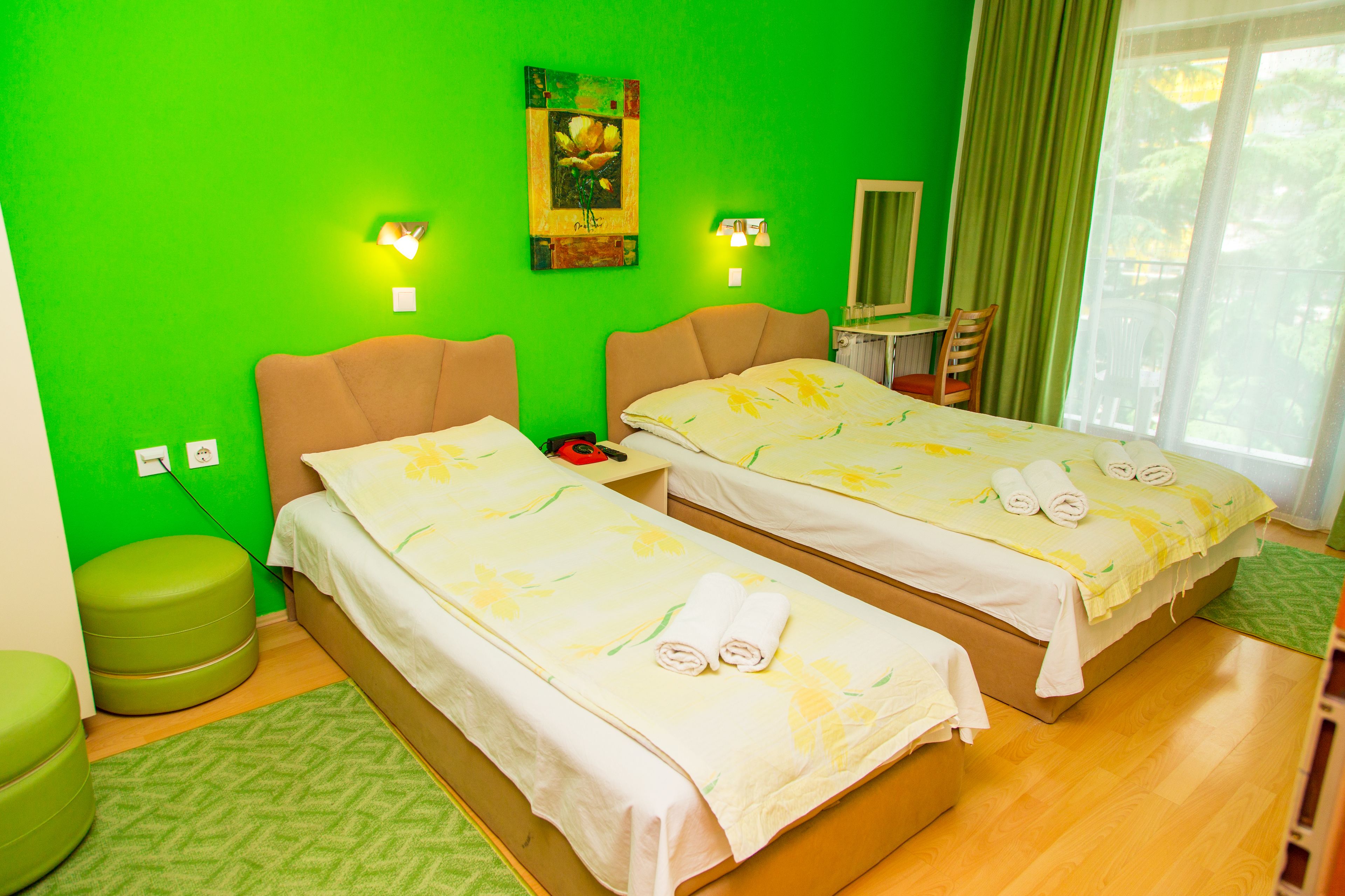 A hotel room with two beds, a green wall, and a view of the outdoors.