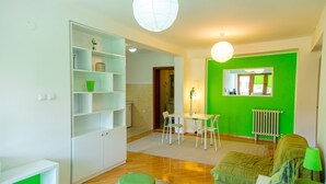 A modern living room with a green accent wall, a dining area with a table and chairs, and a white built-in shelving unit. - Hotel Pine (Skopje)