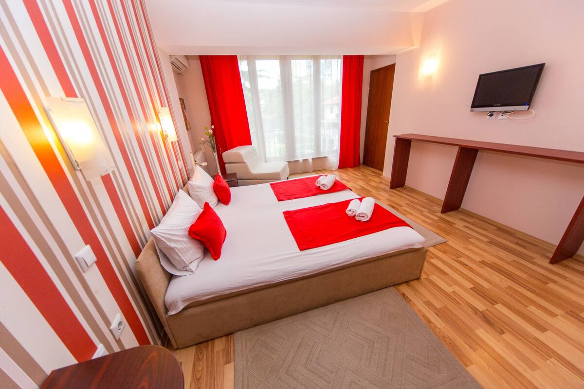 A hotel room with a large bed, a desk, a chair, and a TV on the wall.