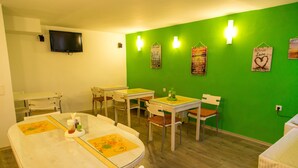 A dining area with multiple tables and chairs, a flat-screen TV mounted on the wall, and decorative wall hangings. - Hotel Pine (Skopje)