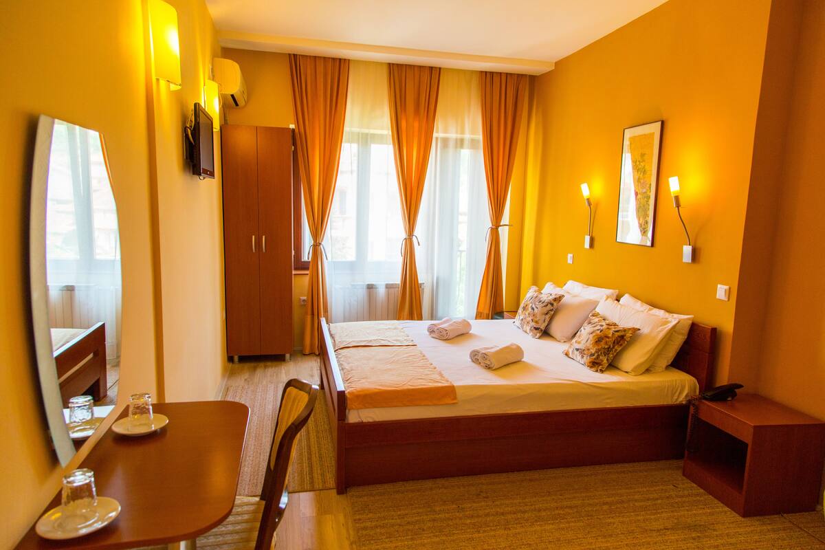 A hotel room with a bed, bedside table, and a mirror.
