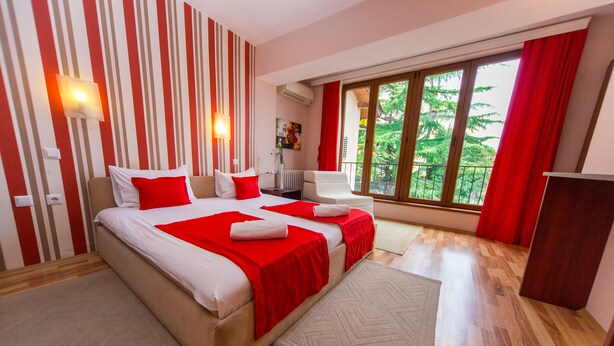 A modern hotel room with a large bed, a desk, and a balcony with a view of trees. - Hotel Pine (Skopje)