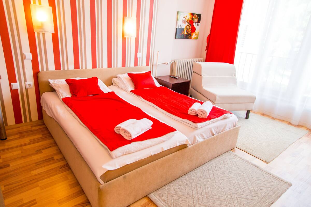 A double bed with red and white bedding, a bedside table, a chair, and a radiator.