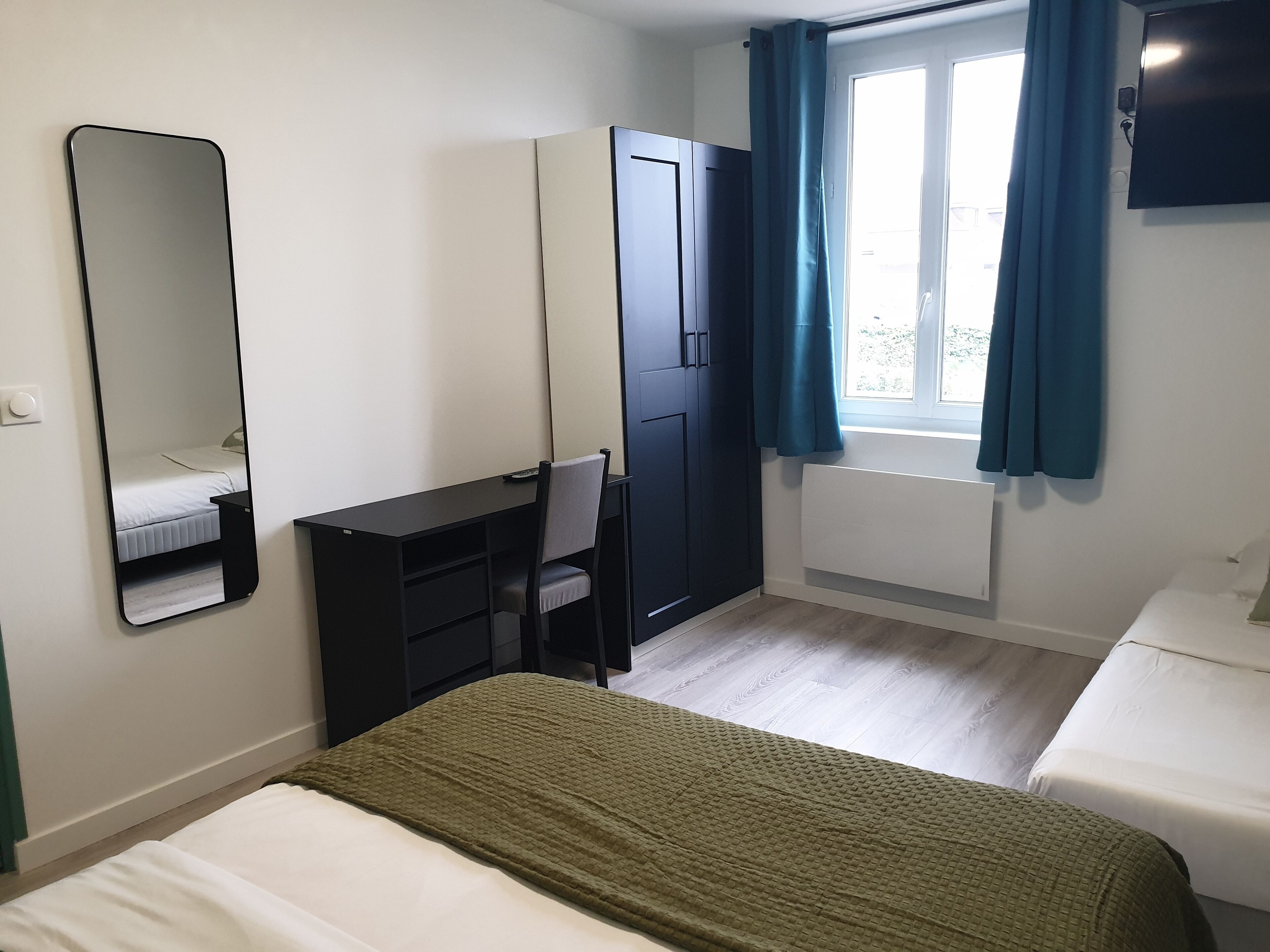 A bedroom with a bed, a desk, a chair, a wardrobe, and a window with curtains.