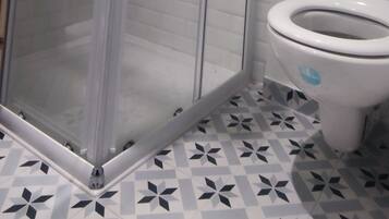 Un baño con ducha de mampara de vidrio, inodoro y baldosas de suelo con diseño.