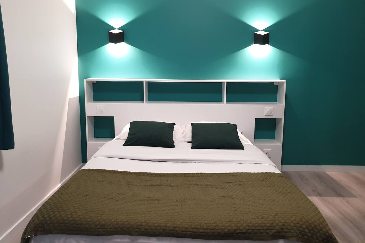 Un lit avec une tête de lit blanche, deux oreillers noirs et une couverture verte.