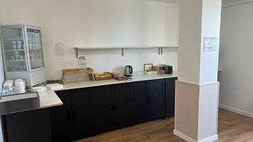 Una kitchenette equipada con refrigerador, microondas y cafetera. Encima del mostrador hay un estante de madera con varios objetos.