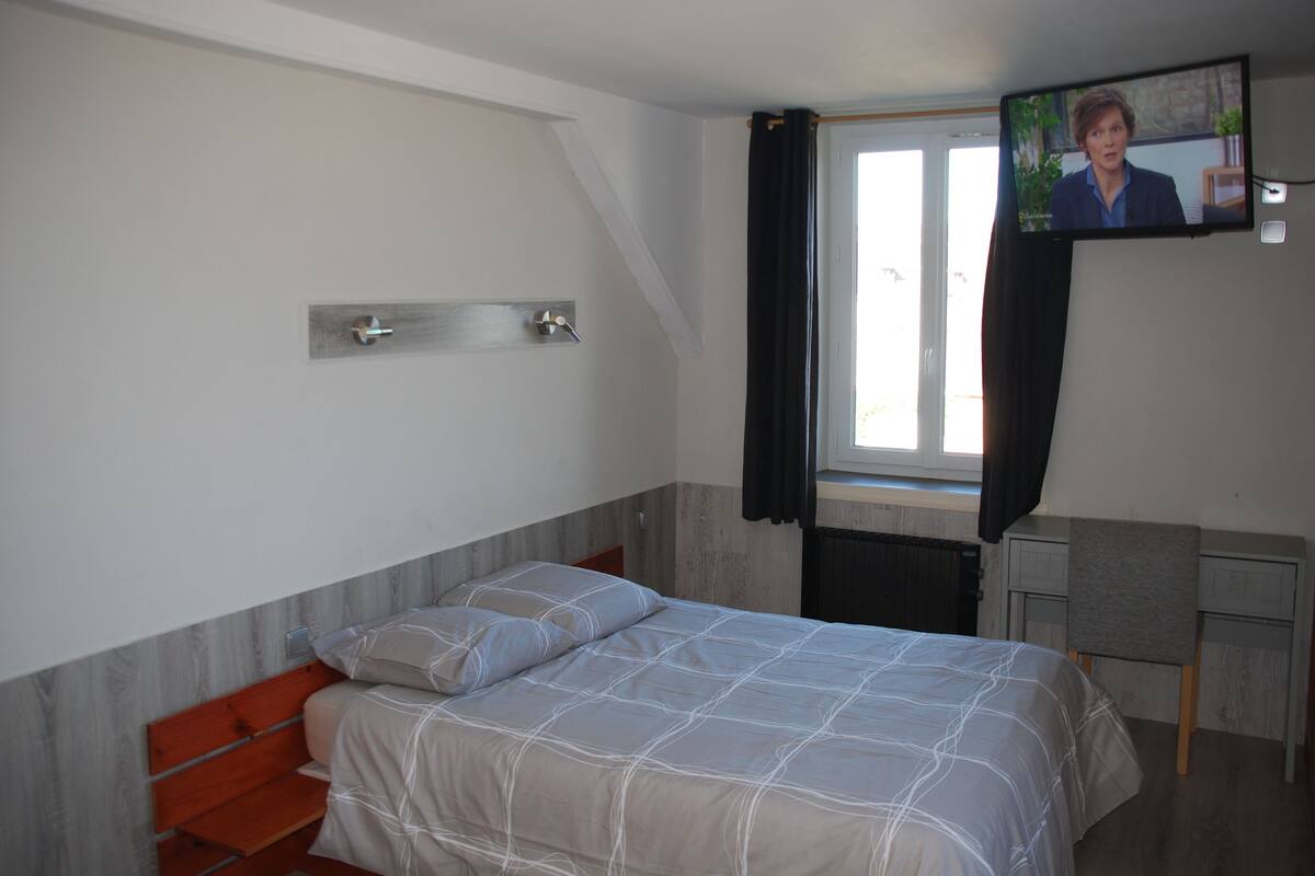Une chambre à coucher avec un lit, un téléviseur fixé au mur, une fenêtre avec des rideaux et un radiateur.