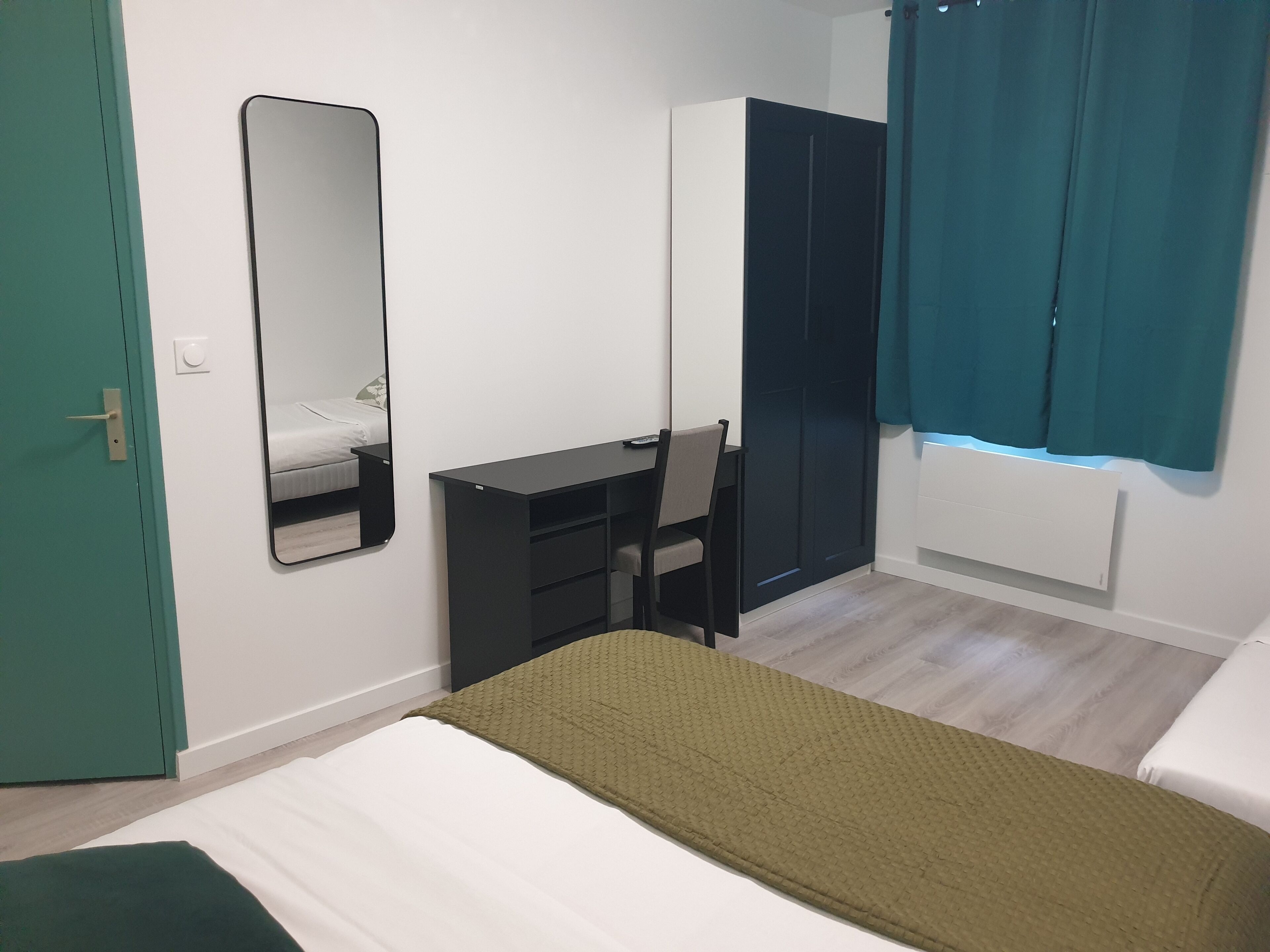 Un dormitorio con cama, escritorio, silla, armario y espejo.