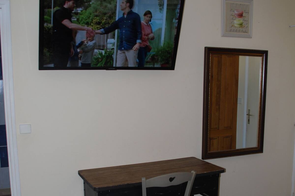 Une chambre à coucher comprenant un lit, un bureau avec une chaise, un téléviseur fixé au mur et un miroir.