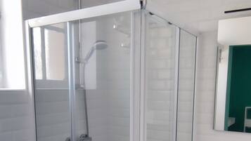 Een moderne badkamer met een douchecabine van glas, een witte wastafel en een spiegel erboven.