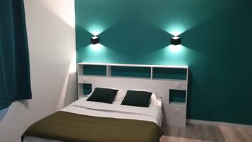 A neatly made bed with a green throw, white bedding, and a white headboard with shelves.