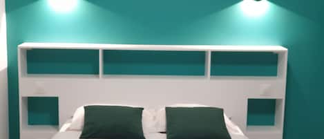 Una cama con cabecera blanca y paredes verde azuladas, dos almohadas verdes y dos lámparas fijadas a la pared.