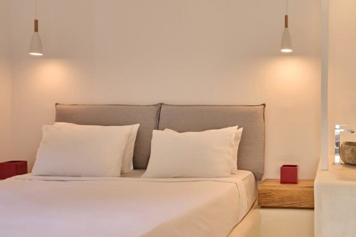 A neatly made bed with a grey headboard, white bedding, and two bedside tables with red and wooden accents.