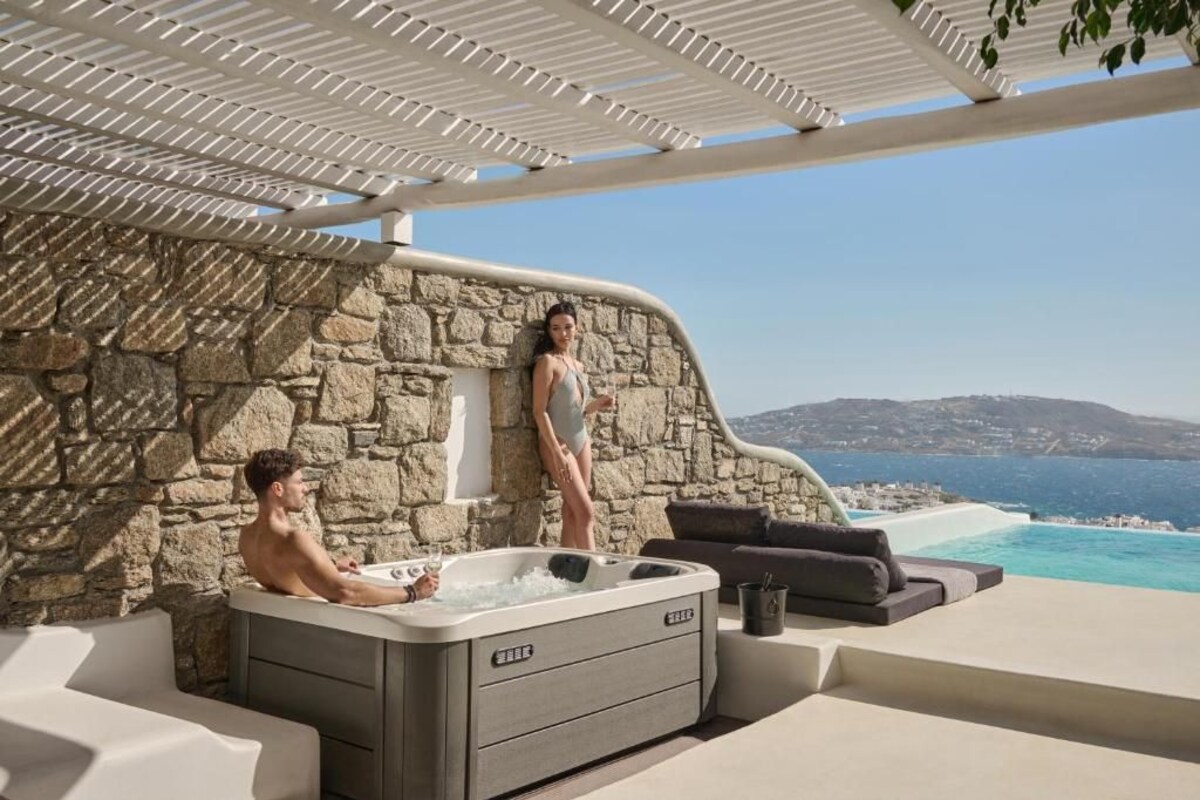 Un jacuzzi con un muro de piedra de fondo y vista al mar, una persona de pie.