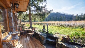 Eine Holzterrasse mit Steinmauern, Sitzgelegenheiten im Freien und Blick auf einen bewaldeten Hügel.