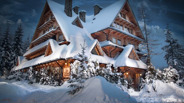 Eine große, mehrstöckige Blockhütte mit einem steilen Dach, umgeben von schneebedeckten Bäumen.