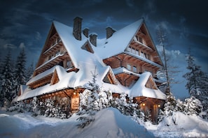 A large, multi-story log cabin with a steeply pitched roof, surrounded by snow-covered trees. - Willa Przy Dolinie Kościeliskiej (Koscielisko)