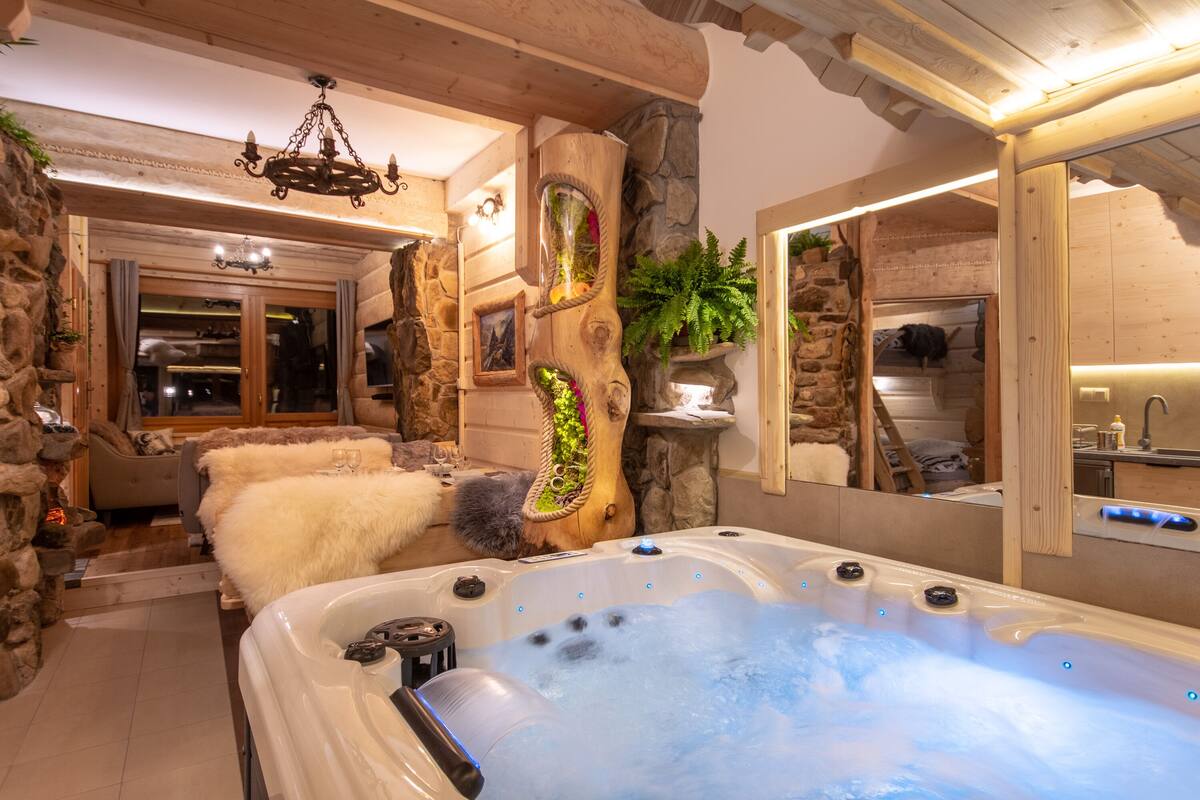 A spa area with a hot tub, stone walls, wooden beams, and a mirror reflecting the room.