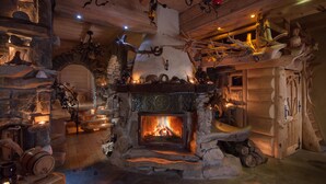 Ein rustikaler Kamin aus Stein mit Feuer, umgeben von Holzdekoration und Geweihen.