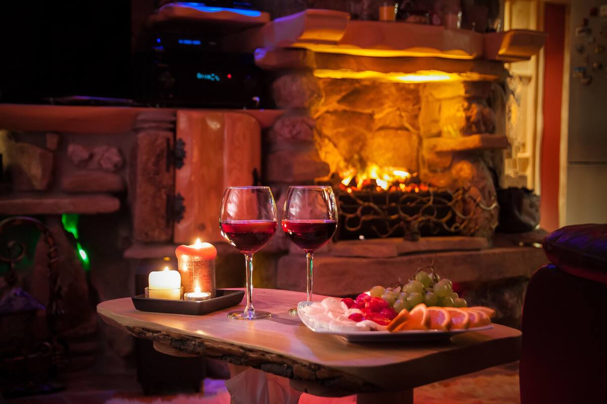 A table with two glasses of red wine, a candle, and a plate of fruit.
