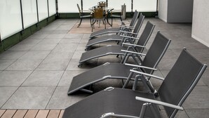 A rooftop terrace with sun loungers and a table, overlooking a body of water. - Hotel Campo (Renningen)