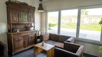Ein Wohnzimmer mit Holzschrank, braunem Ledersofa, Holztisch und großem Fenster mit Blick ins Grüne.