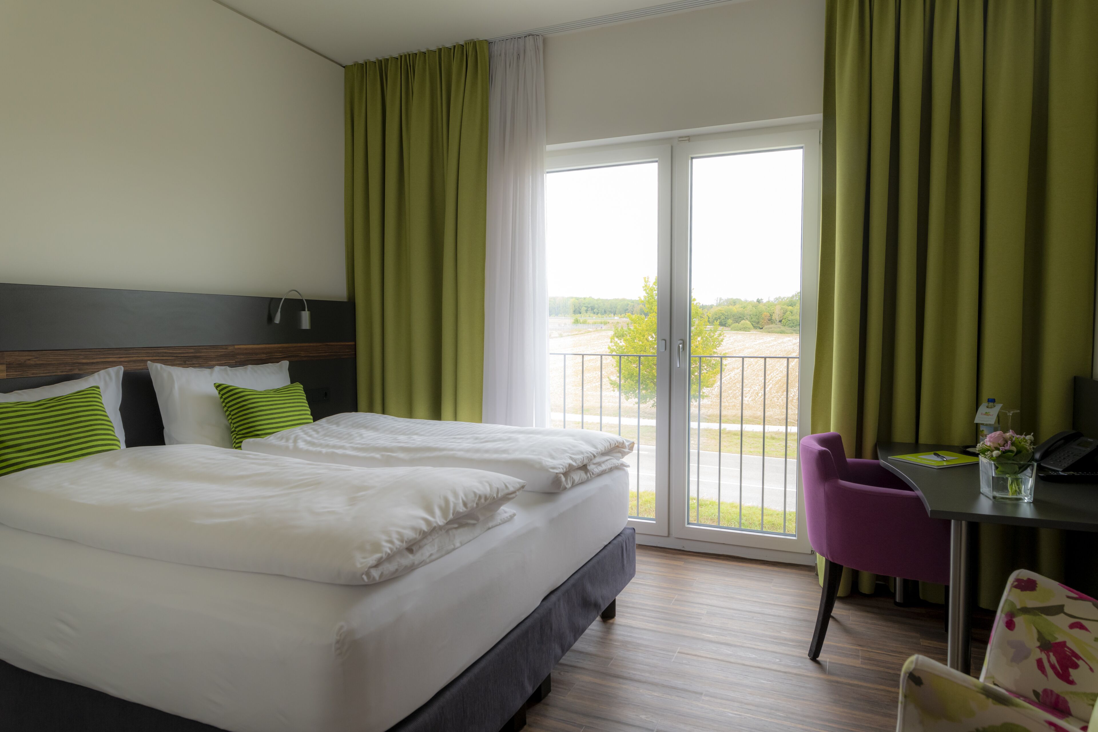 A hotel room with a bed, a desk, a chair, and a view of the outdoors.