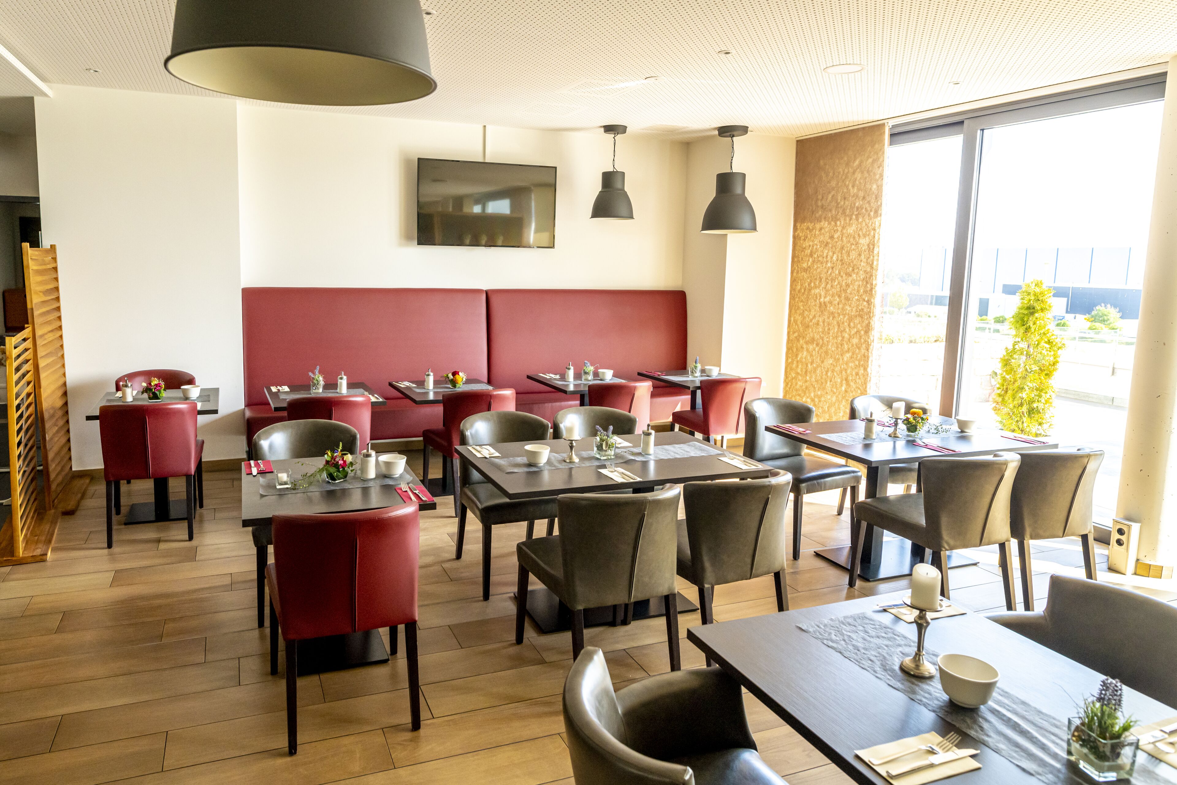 A restaurant with red booths and tables, wooden flooring, and pendant lighting.