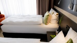 A hotel room with a bed, pillows, a nightstand, a bottle of wine, and a vase with flowers. - Hotel Campo (Renningen)