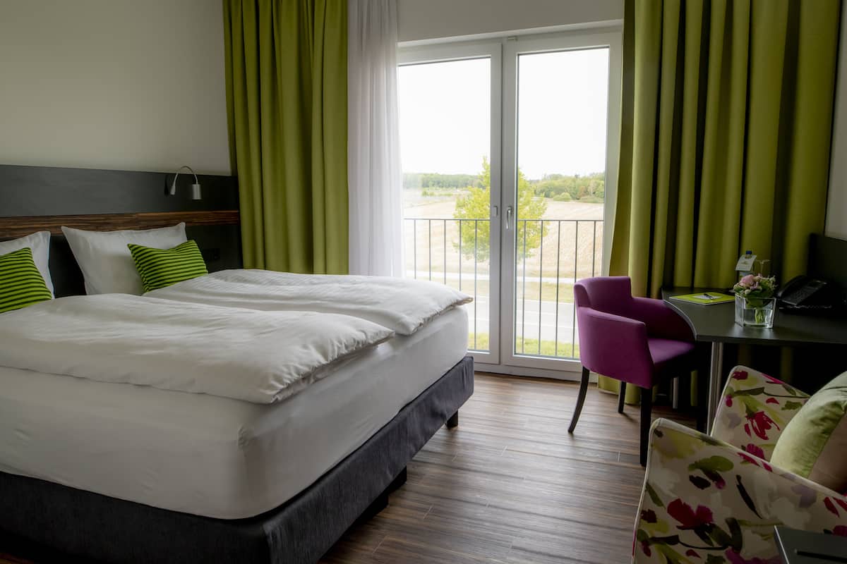 A hotel room with a large bed, a desk with a chair, and a balcony with a view.
