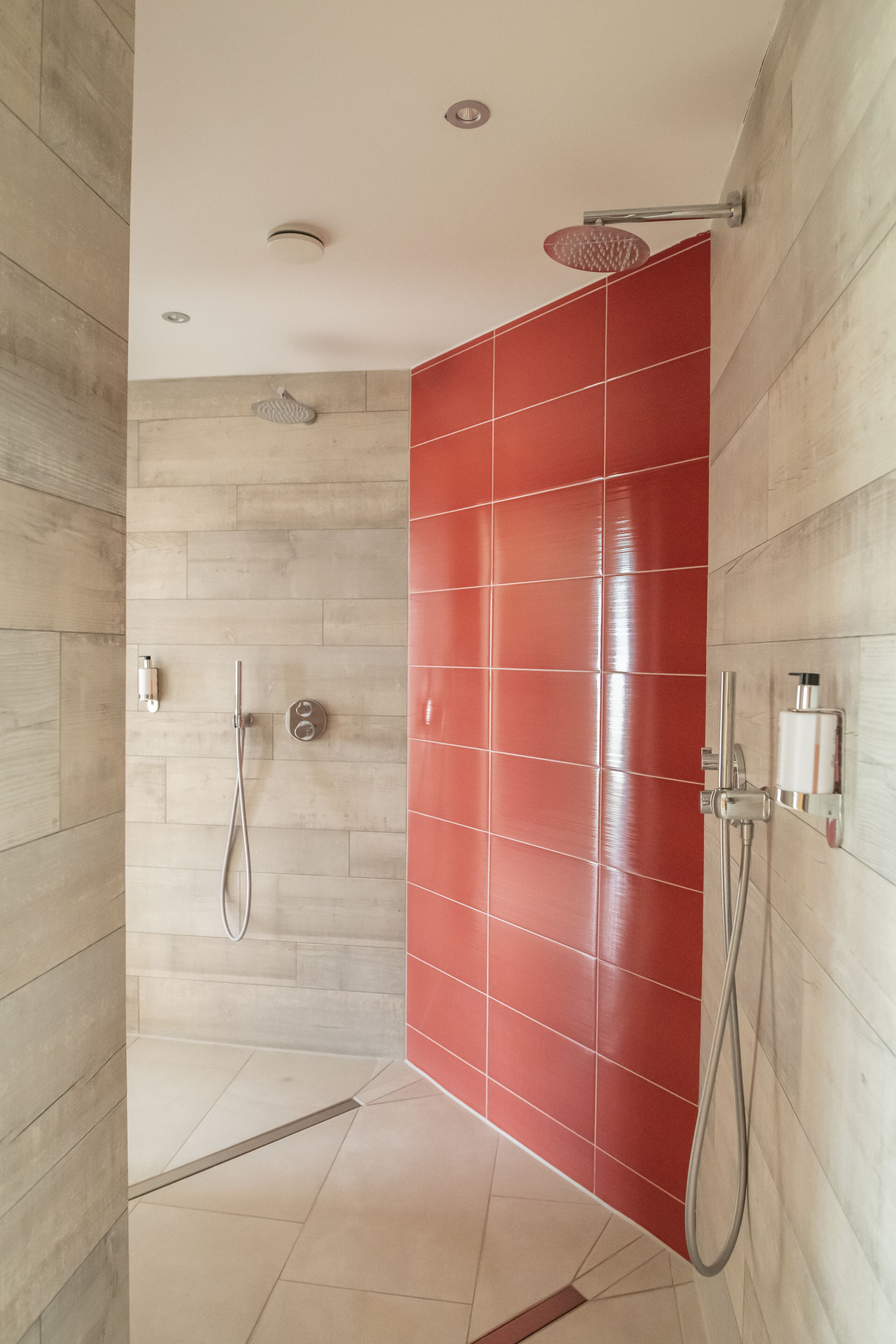 Ducha con cabezal de ducha de mano y grifo de pared, con azulejos en rojo y beige.