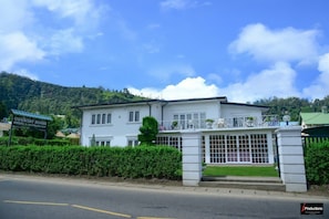 Edificio blanco de dos pisos con entrada protegida por una reja, un letrero que dice "COUNTRY HOUSE" y montañas al fondo.