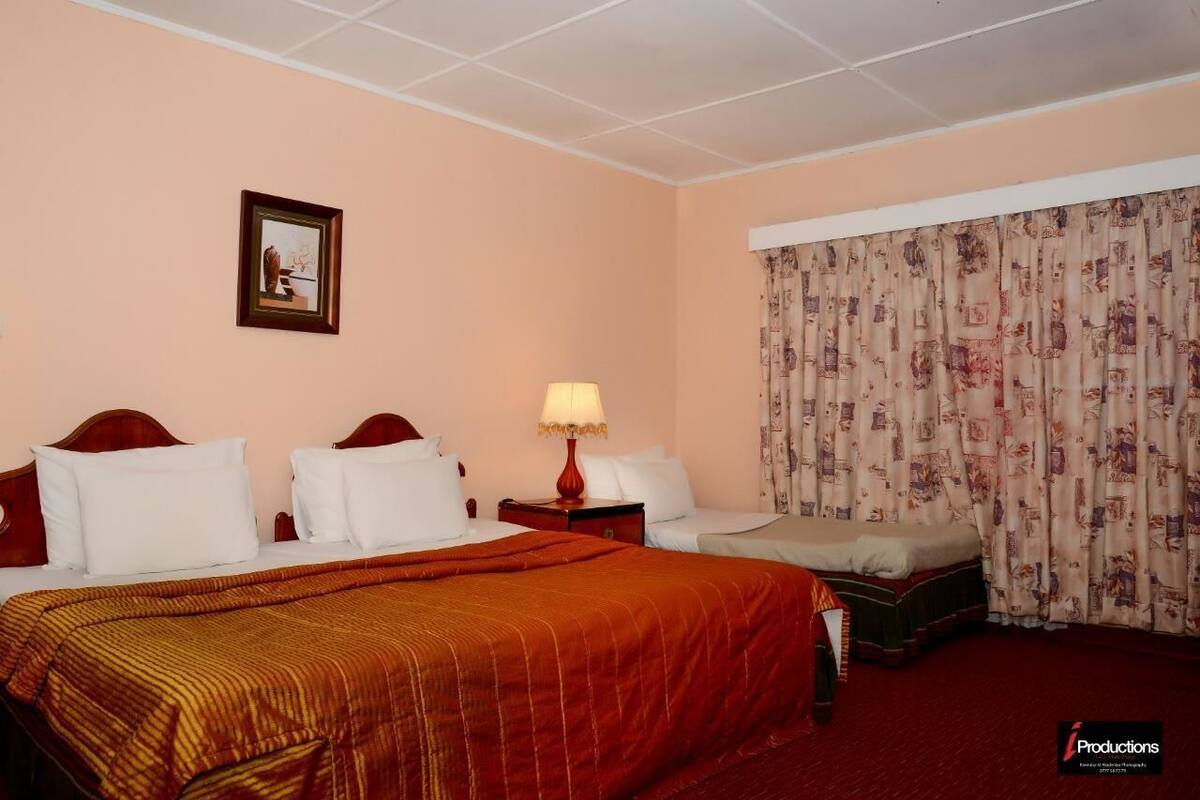 A hotel room with a large bed, two bedside tables, a nightstand, and a window with patterned curtains.