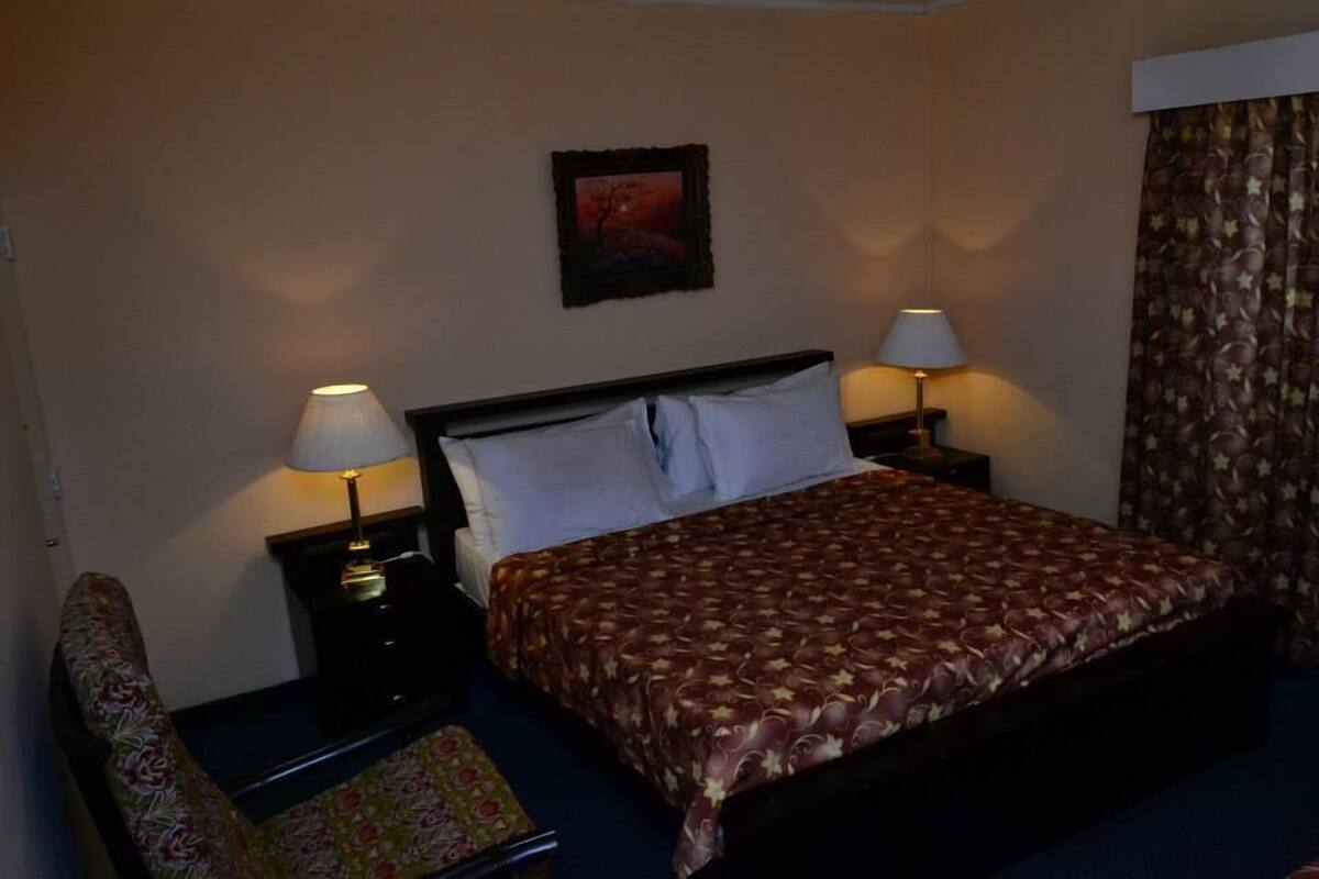 A hotel room with a bed, two bedside tables with lamps, a chair, and a framed picture on the wall.