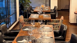 Restaurante com mesas postas para refeições, cadeiras de couro preto e iluminação pendente.