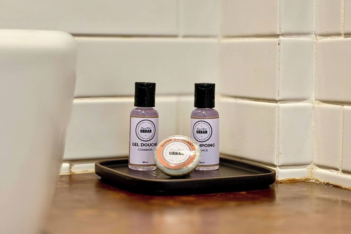 A bathroom corner with white tiles, two bottles of Urban gel douche, and a round soap dish.