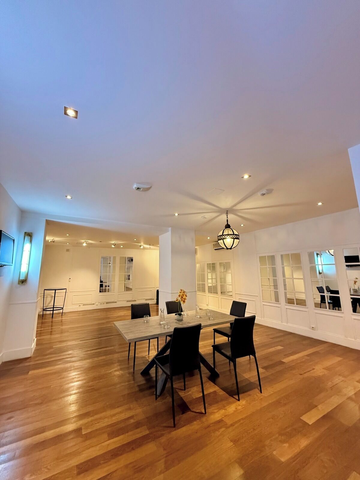A spacious room with a large dining table, black chairs, and a hanging light fixture.